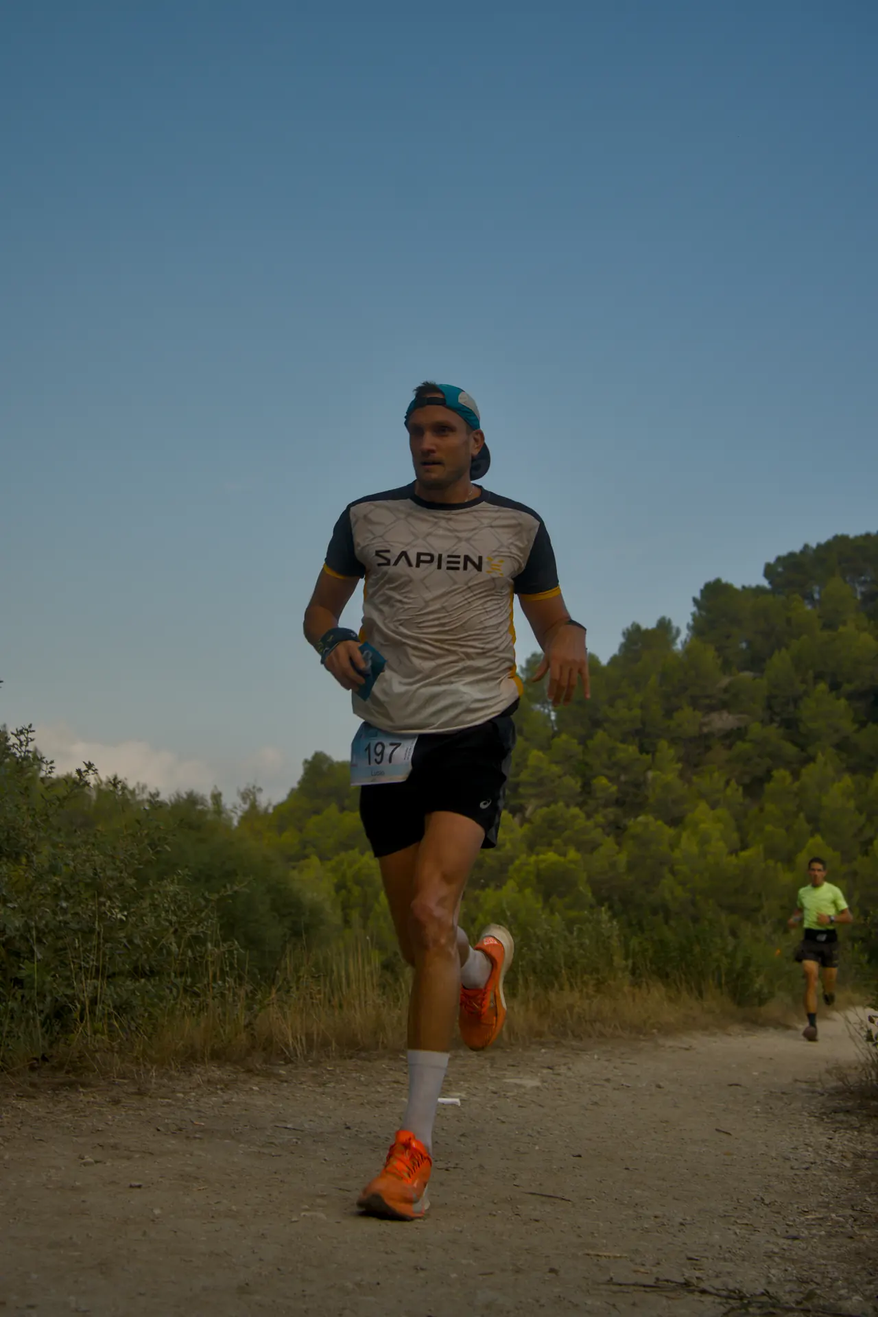 Un coureur en casquette, vu en contre-plongée, s’élance sur un sentier au lever du jour.
