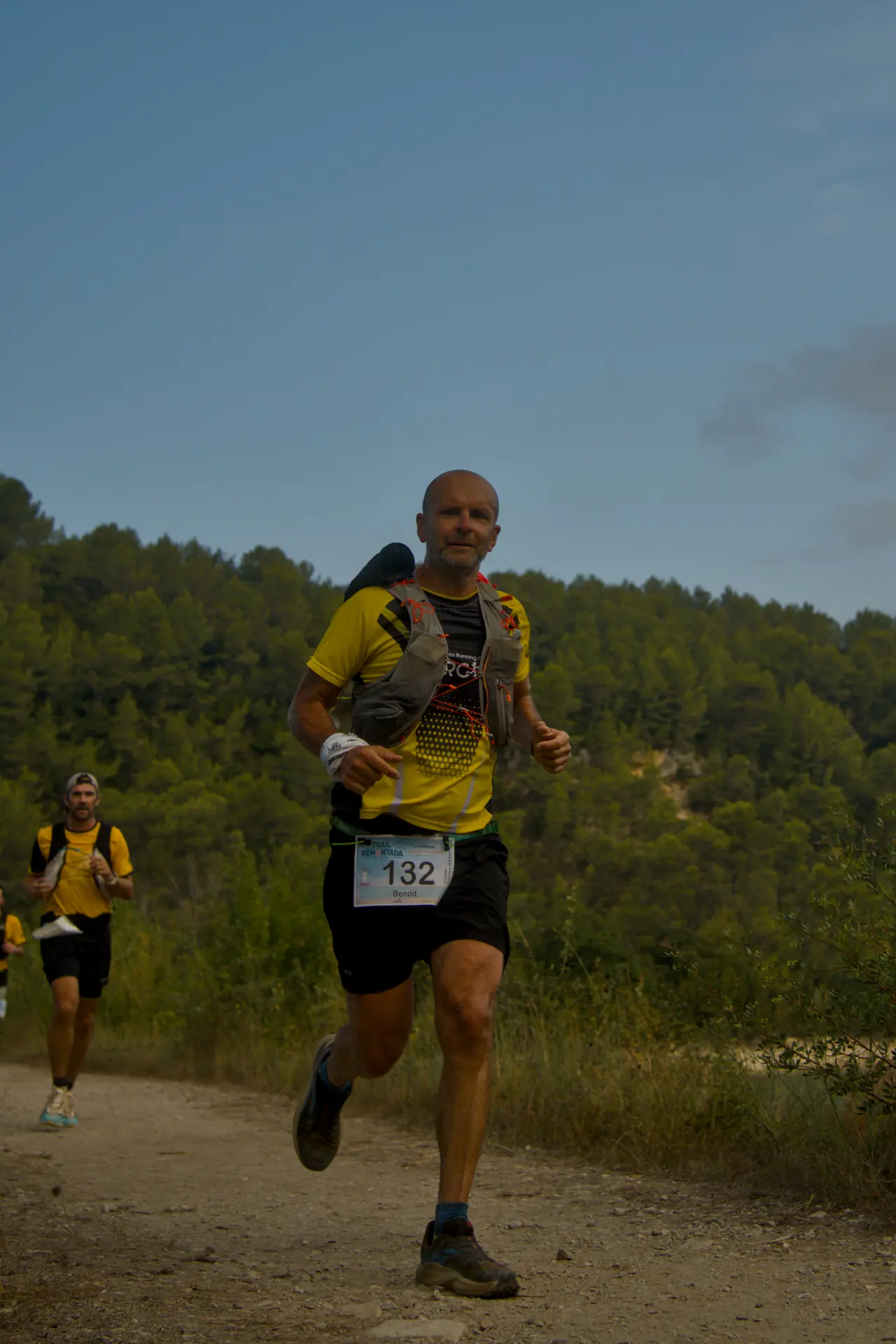 Un coureur en maillot jaune mène un petit groupe sur le sentier.
