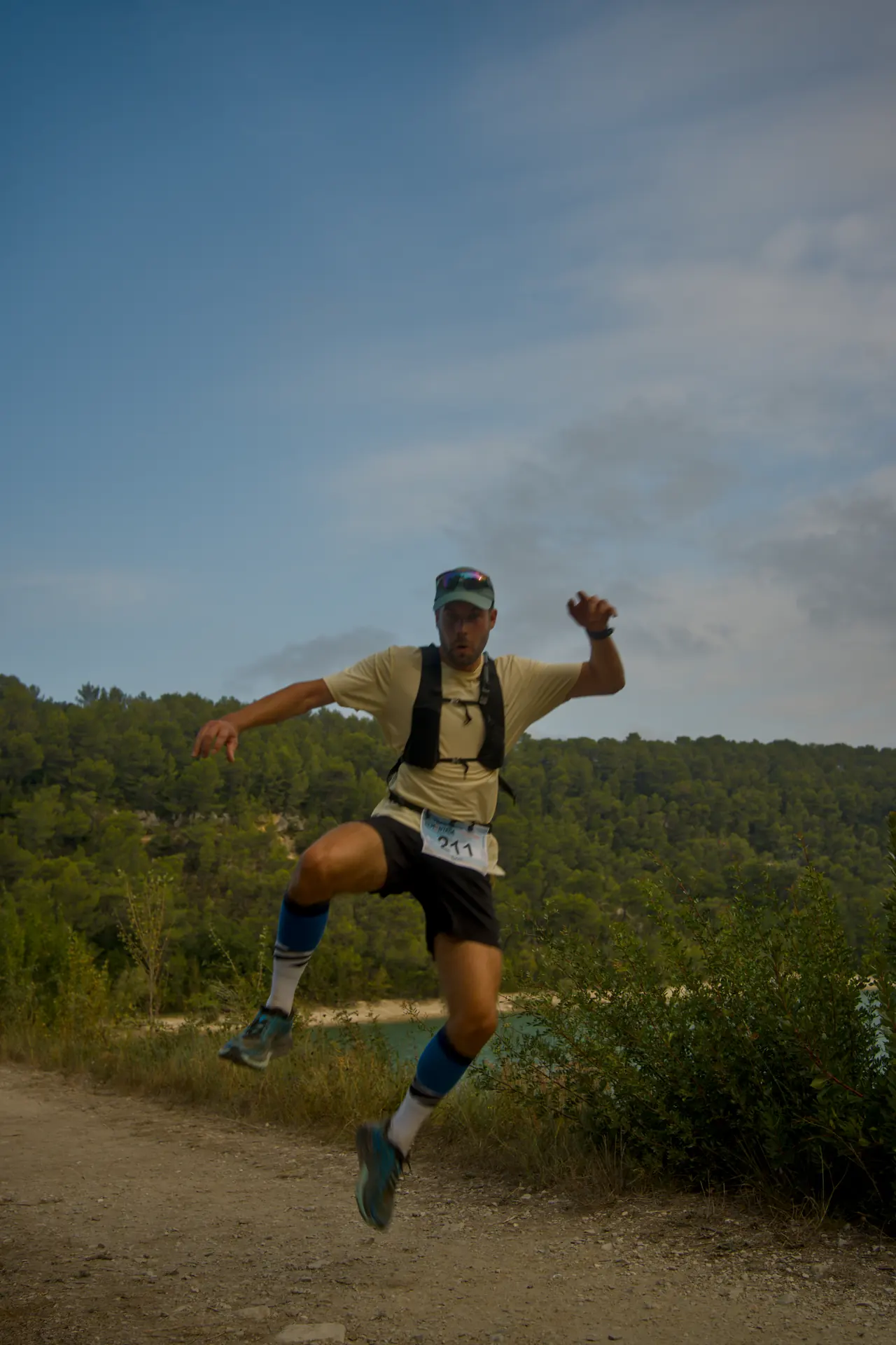 Un coureur saute en l’air au-dessus du sentier, bras écartés.