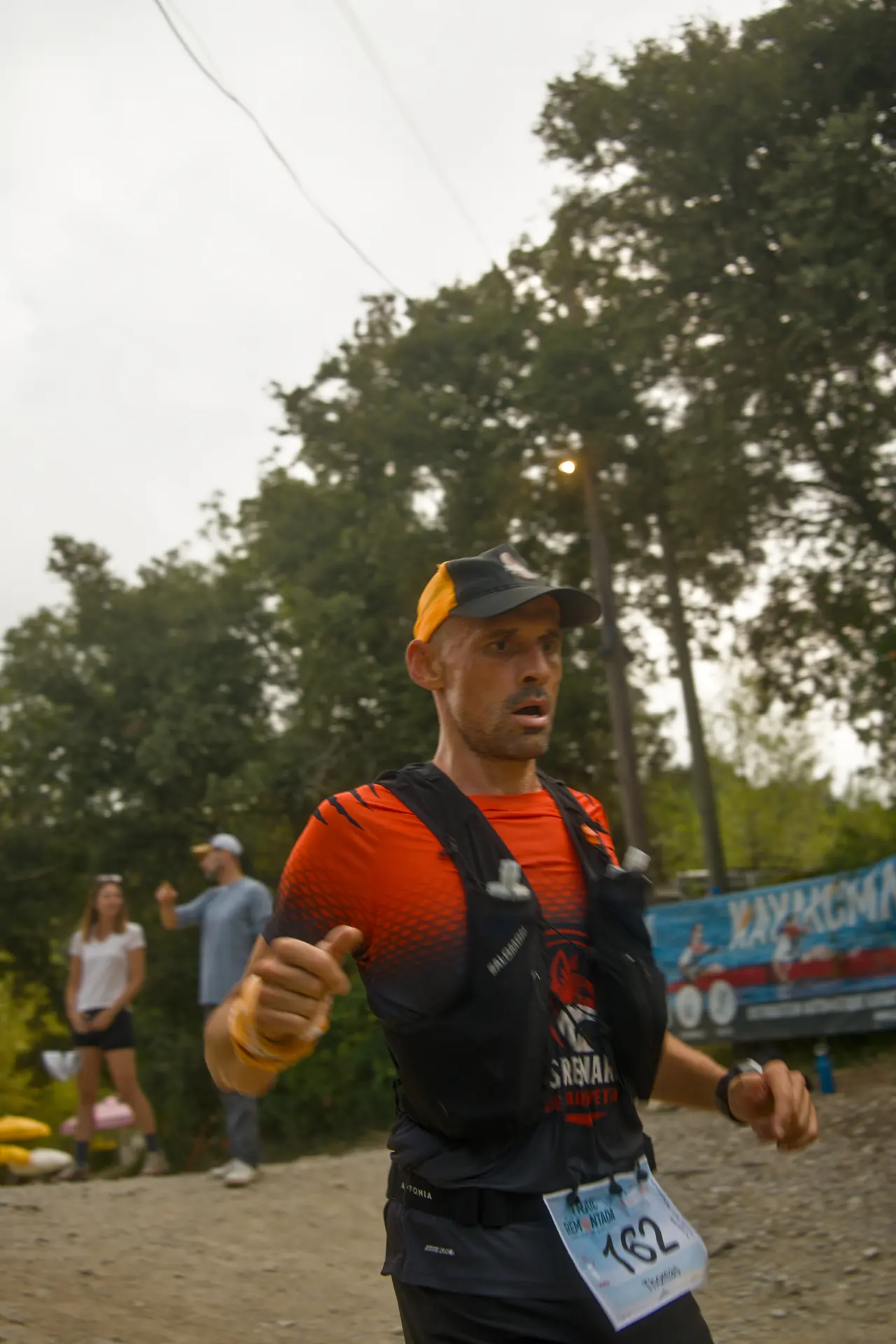 Un coureur concentré, pouce levé, passe devant les spectateurs et la banderole de la course.